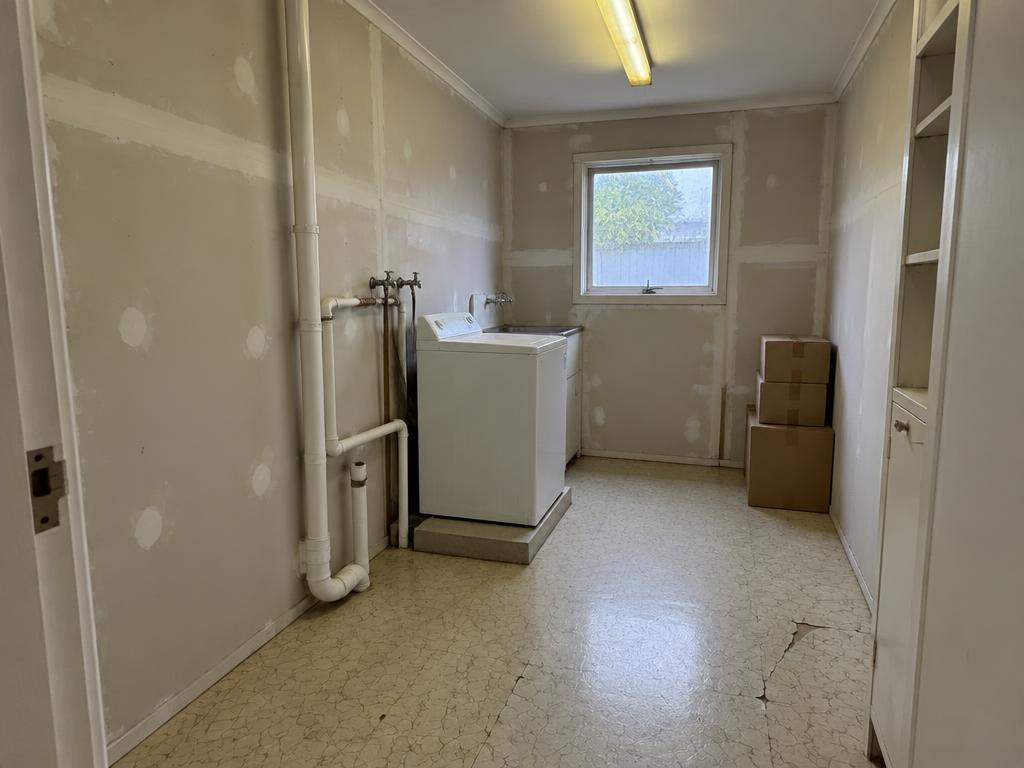 Laundry nook before renovation with exposed pipes and a bare plasterboard wall